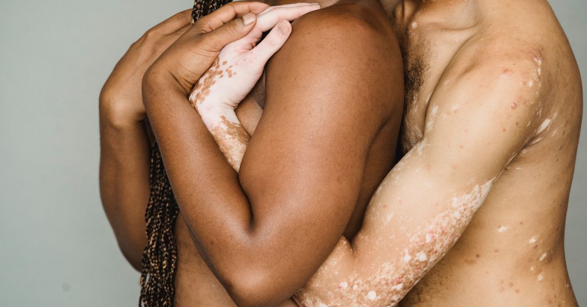 Crop anonymous homosexual diverse friends with naked torso cuddling on gray background of studio